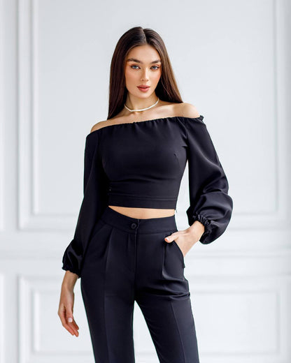 Woman wearing a black off-shoulder top and black pants against a white background