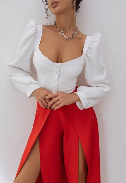 Woman wearing a white blouse with puffed sleeves and a red skirt against a plain background