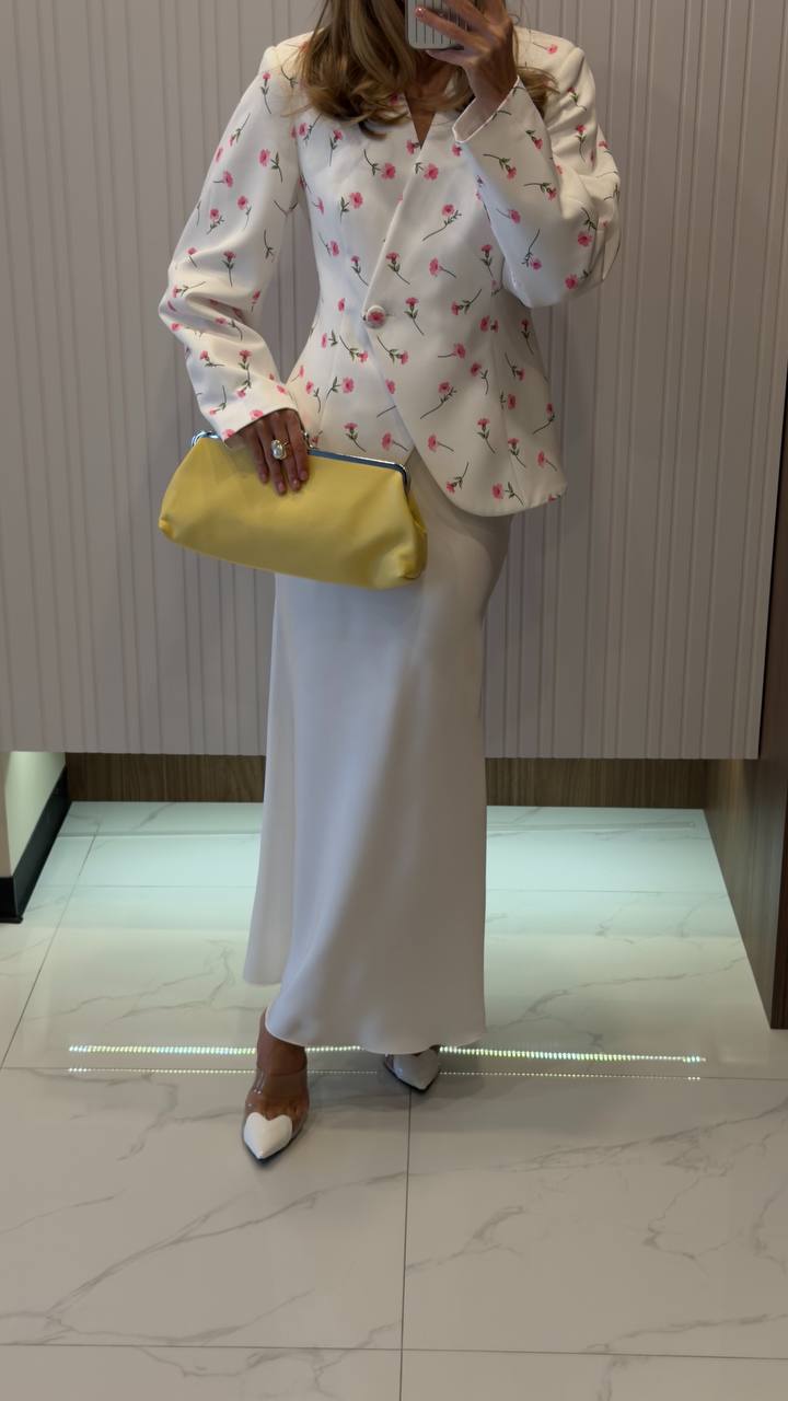 Person wearing a white floral blouse and light-colored pants, holding a yellow clutch.