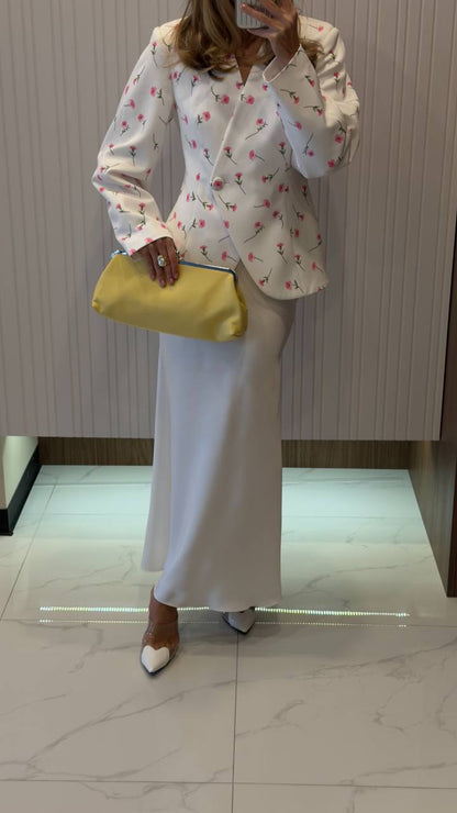 Person wearing a white floral blouse and light-colored pants, holding a yellow clutch.