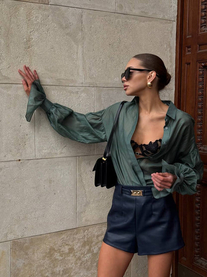 Woman in green jacket and black shorts posing against a stone wall.