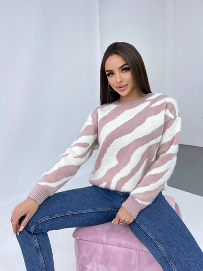 Woman wearing a pink and white striped sweater and blue jeans sitting on a pink stool.