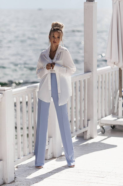 Woman in a white shirt and light blue pants standing on a wooden deck with a blurred background