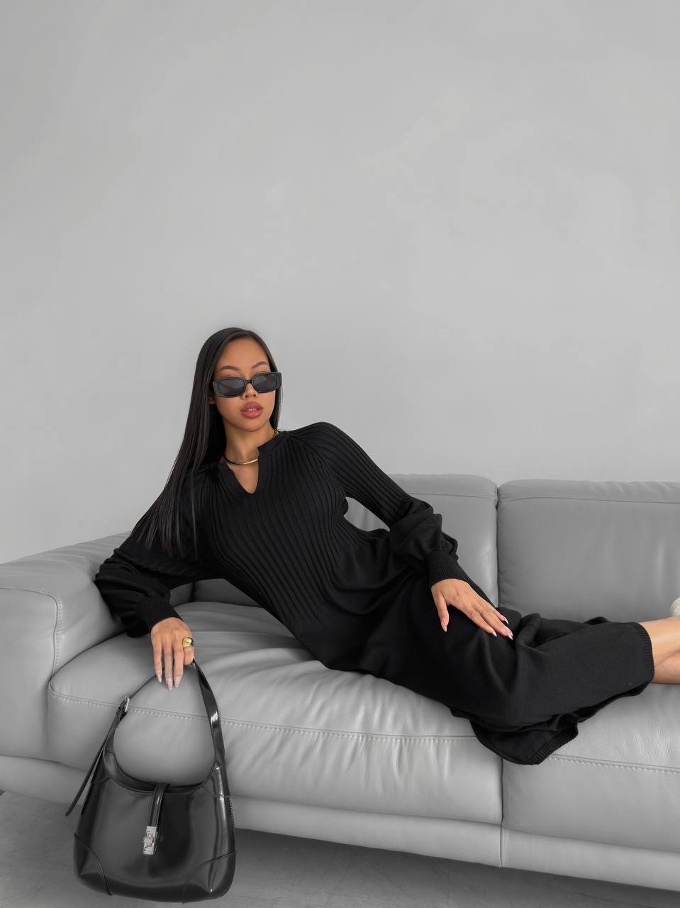 Woman in black outfit sitting on a gray couch with a gray background