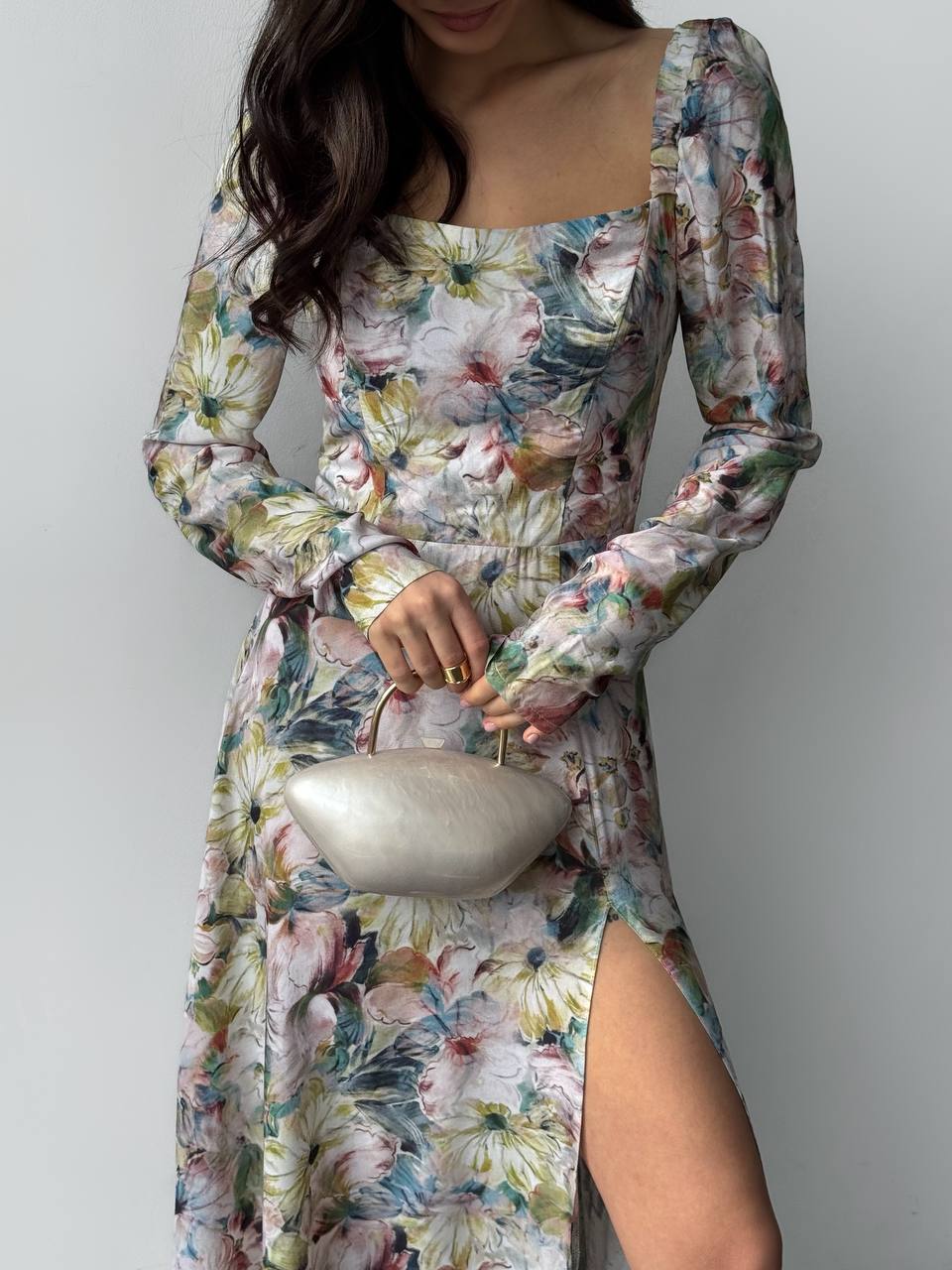 Woman wearing a floral dress holding a silver handbag against a plain background