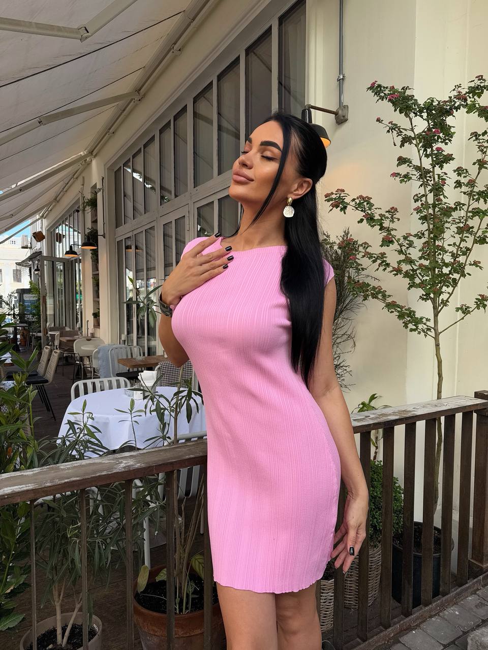 Woman in a pink dress standing on a patio with plants and tables in the background