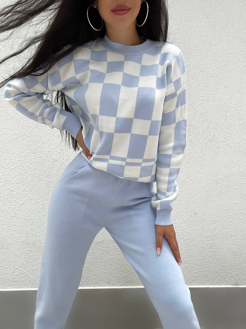 Person wearing a blue and white checkered sweater and pants against a plain background