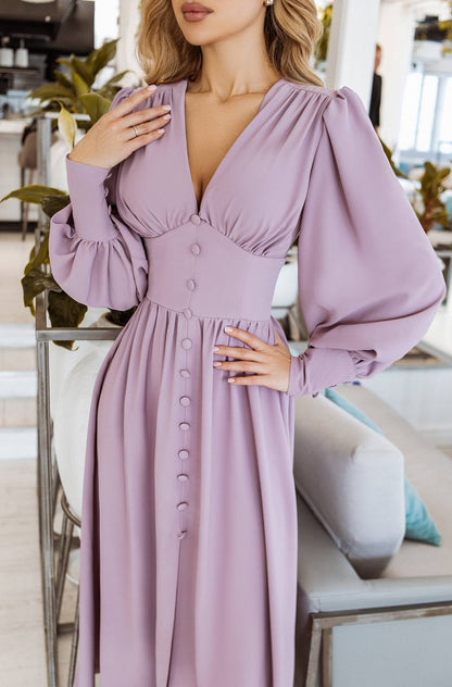 Woman wearing a long, light purple dress with puffed sleeves in an indoor setting.