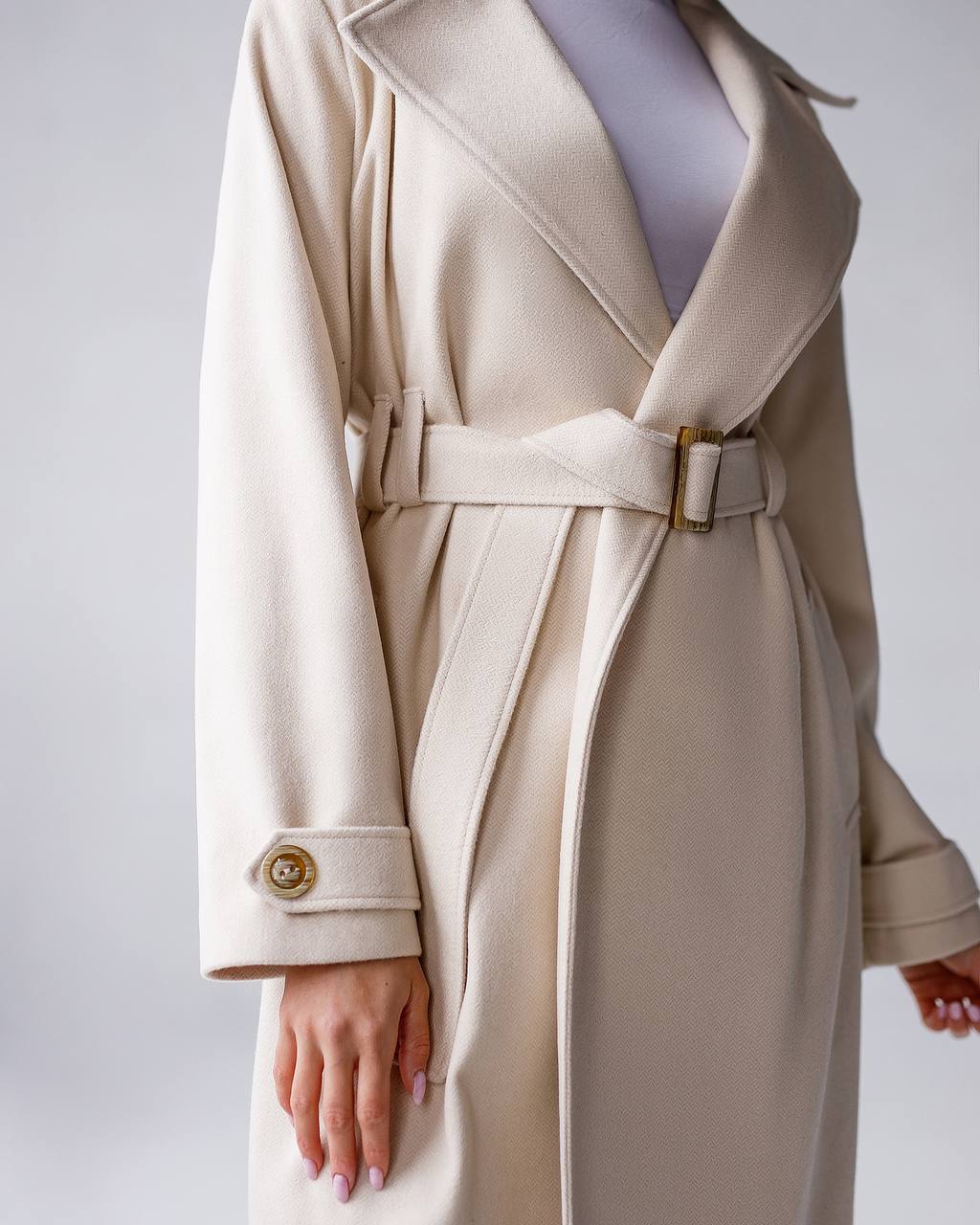 Beige trench coat with a belt on a plain background