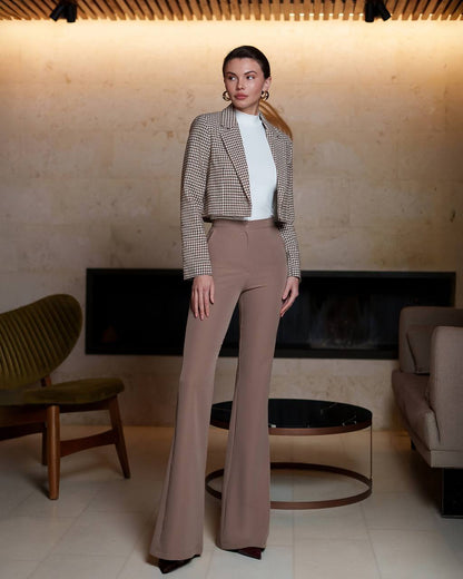 Woman in a checkered blazer and brown pants standing in a modern living room.