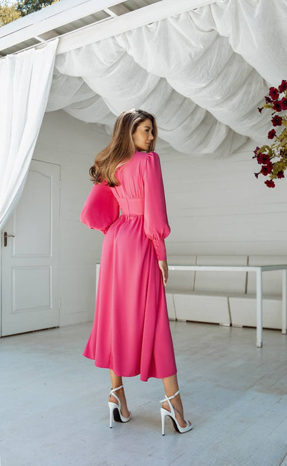 Woman in a pink dress standing in a bright, minimalistic room with white walls and a white door.