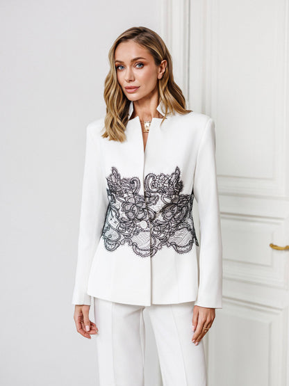 Woman wearing a white blazer with black lace detailing in front of a white door.