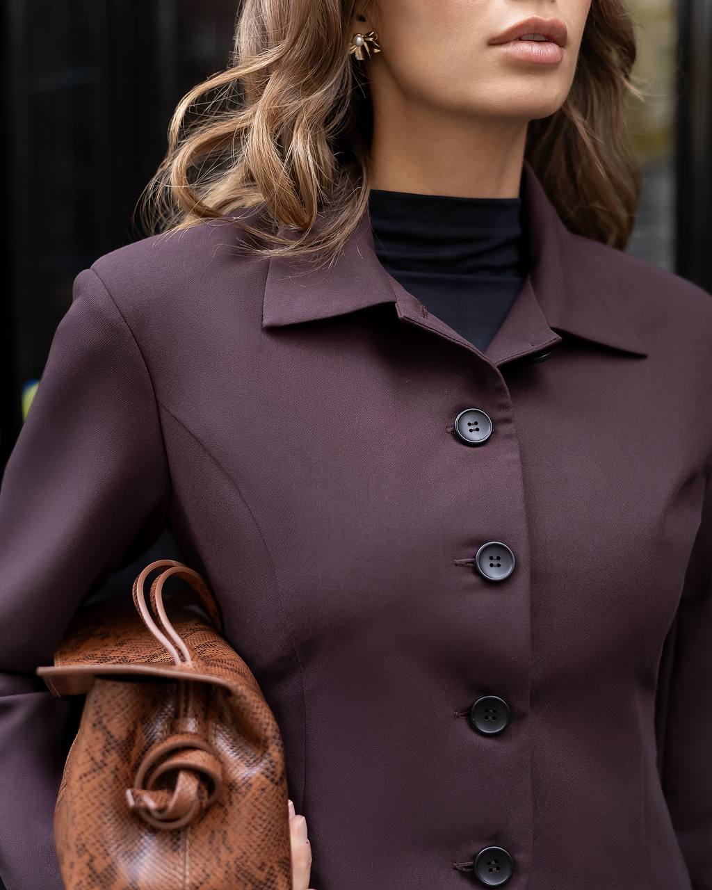 Person wearing a dark purple coat with buttons, holding a brown leather bag.