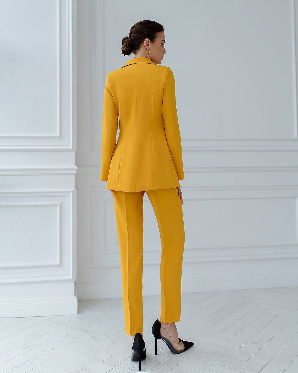 Woman wearing a yellow suit standing in a room with white paneled walls.
