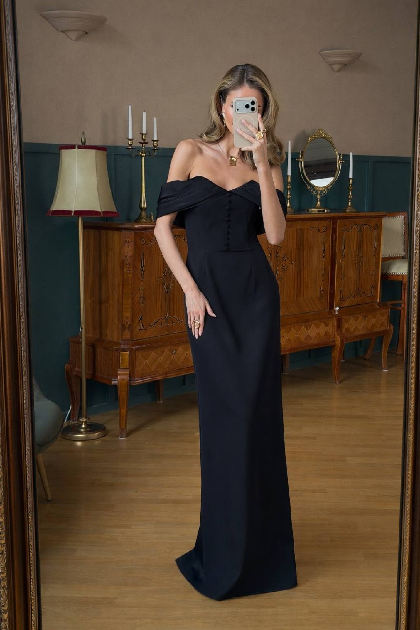 Woman in a black off-shoulder gown taking a mirror selfie in an elegant room.
