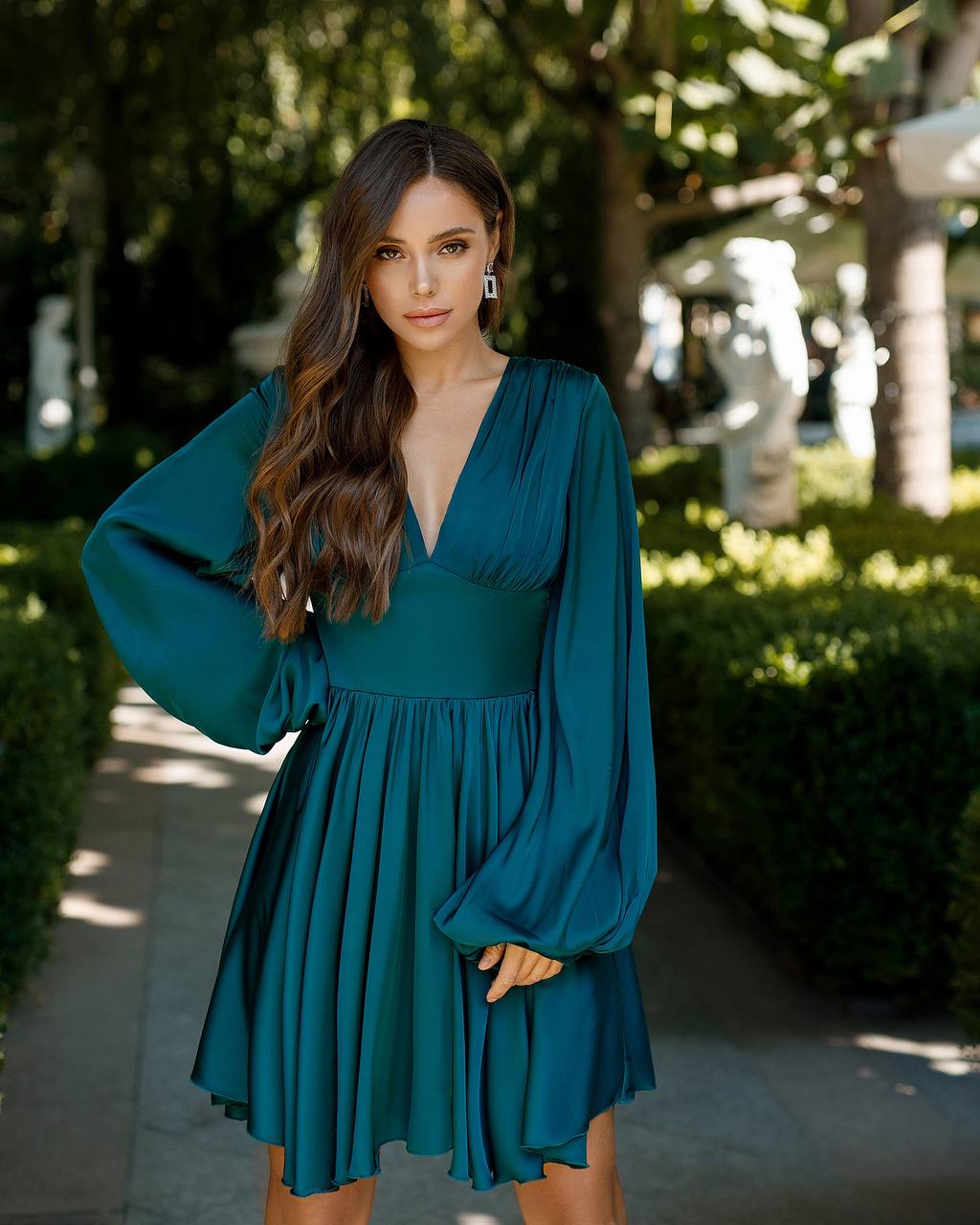 Woman wearing a teal dress standing outdoors with greenery in the background
