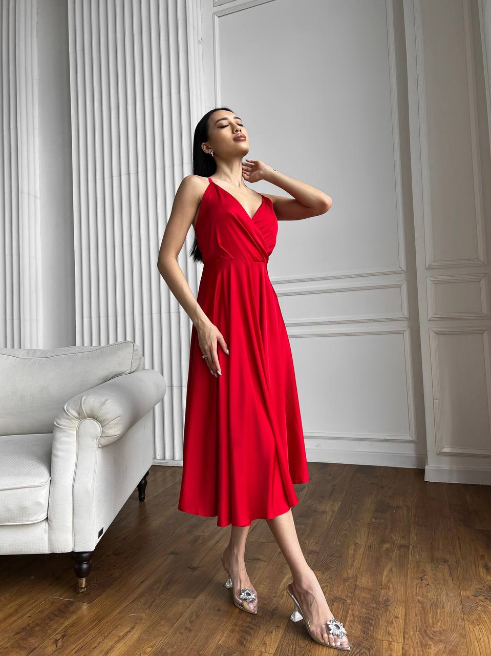 Woman in a red dress standing in a room with white walls and a white sofa.