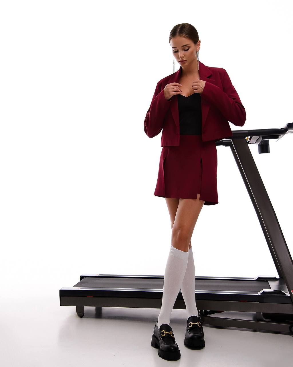 Woman in a red blazer and skirt standing on a treadmill against a white background