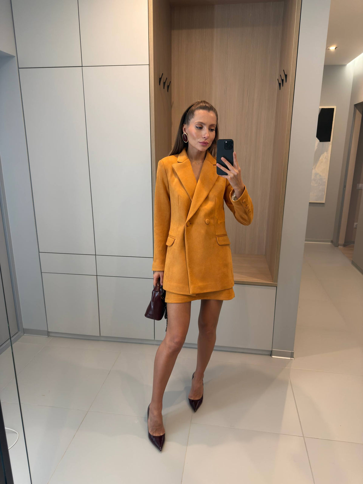 Woman in a mustard yellow suit standing in a modern interior setting.