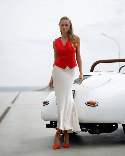 Woman in a red top and white skirt standing next to a vintage car.