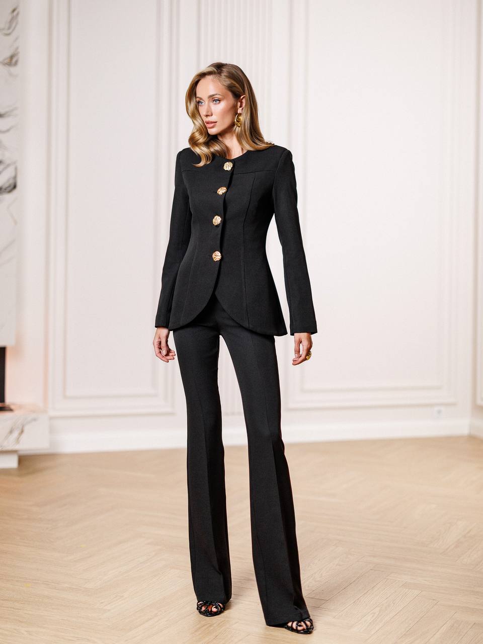 Woman wearing a black suit with gold buttons in an elegant room.