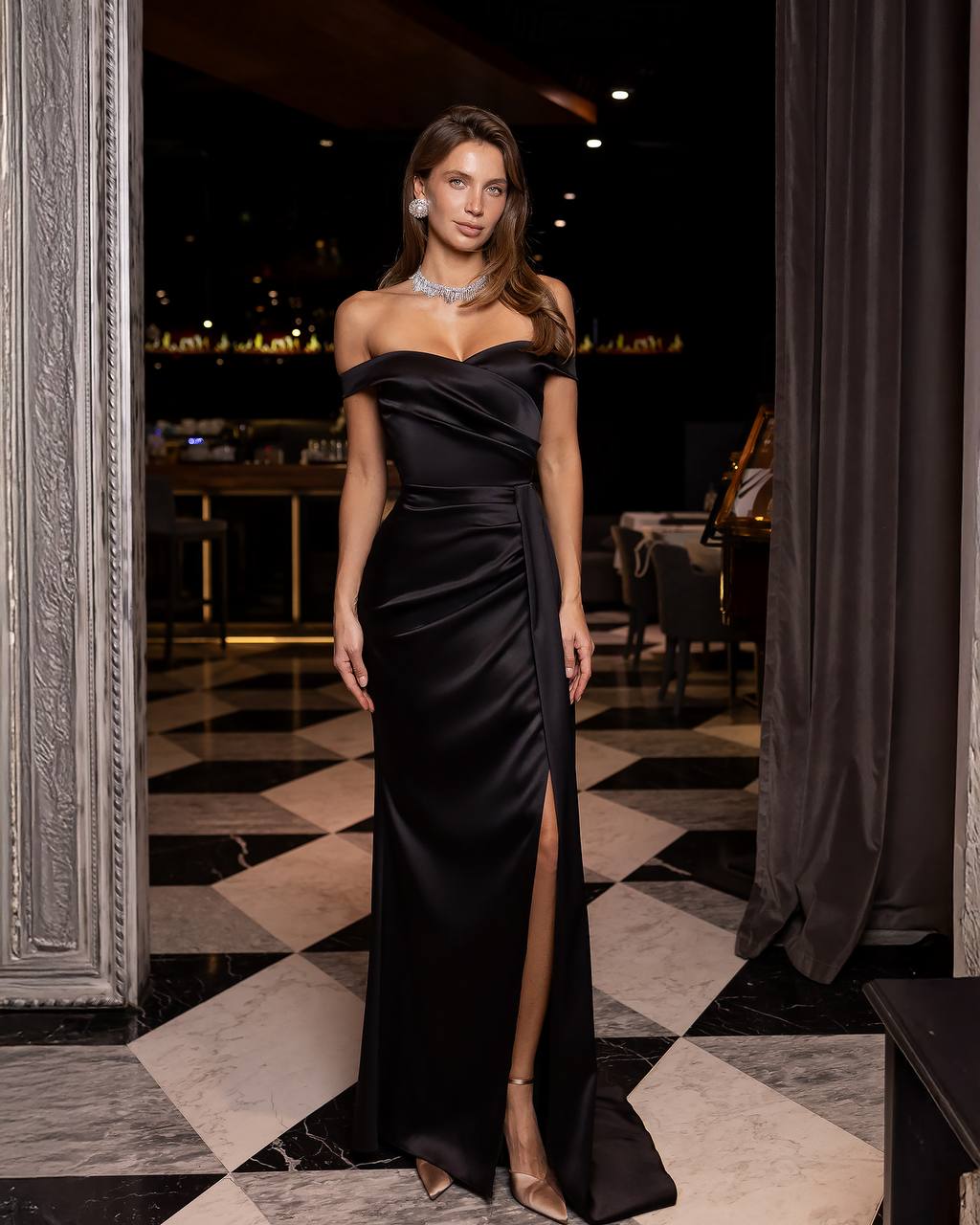 Woman in a black off-shoulder gown standing in an elegant indoor setting.
