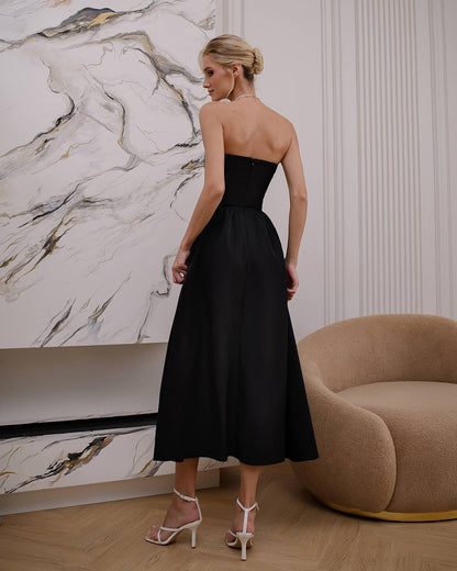 Woman in a black strapless dress standing in a room with marble wall and brown chair.