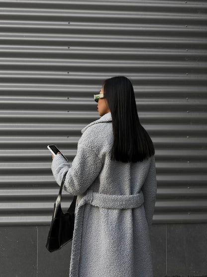 Person wearing a gray coat and holding a phone, standing in front of a metallic shutter.