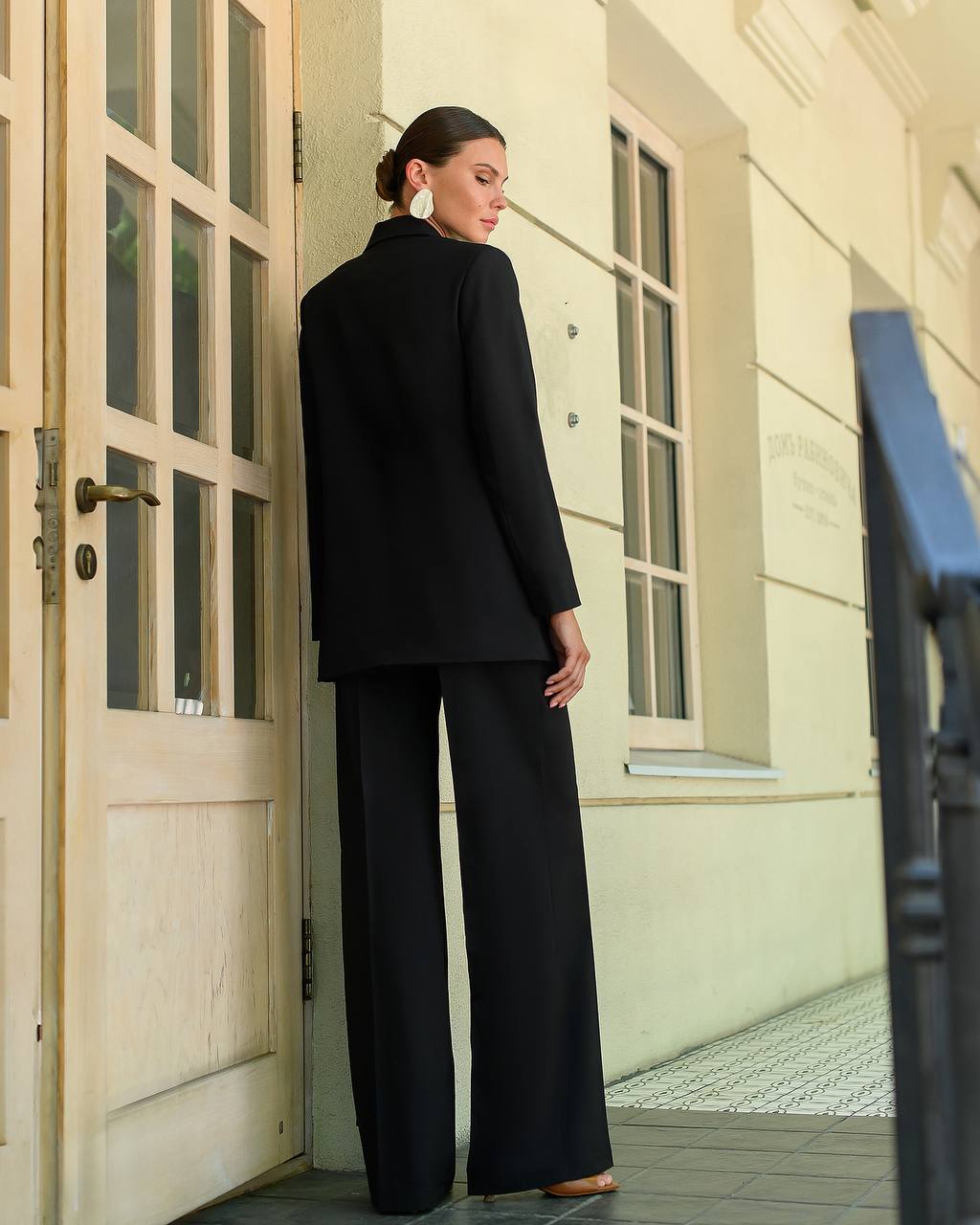 Woman in a black outfit standing in front of a building entrance.