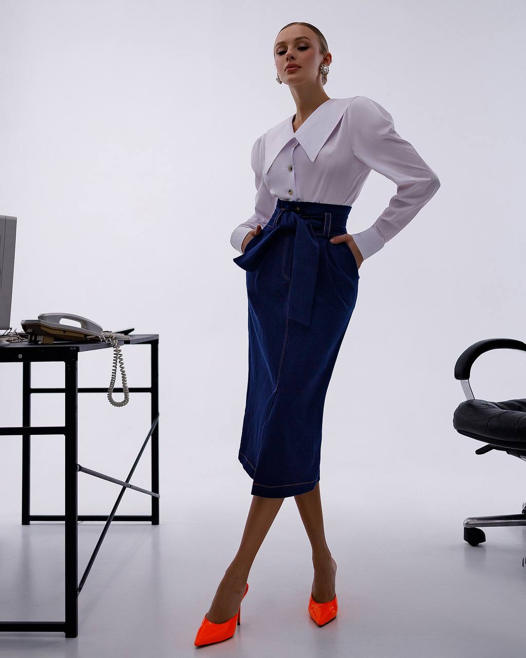 Woman in a white blouse and navy skirt standing in an office setting.