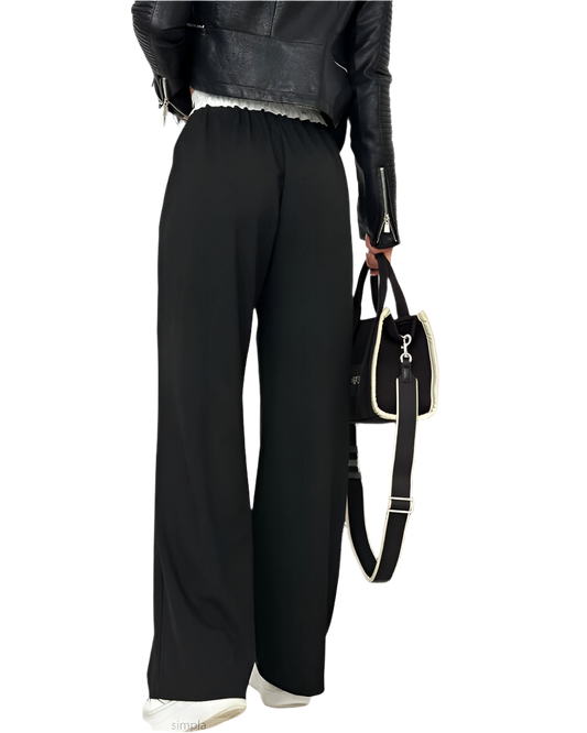 Person wearing black pants and a leather jacket holding a black handbag on a white background