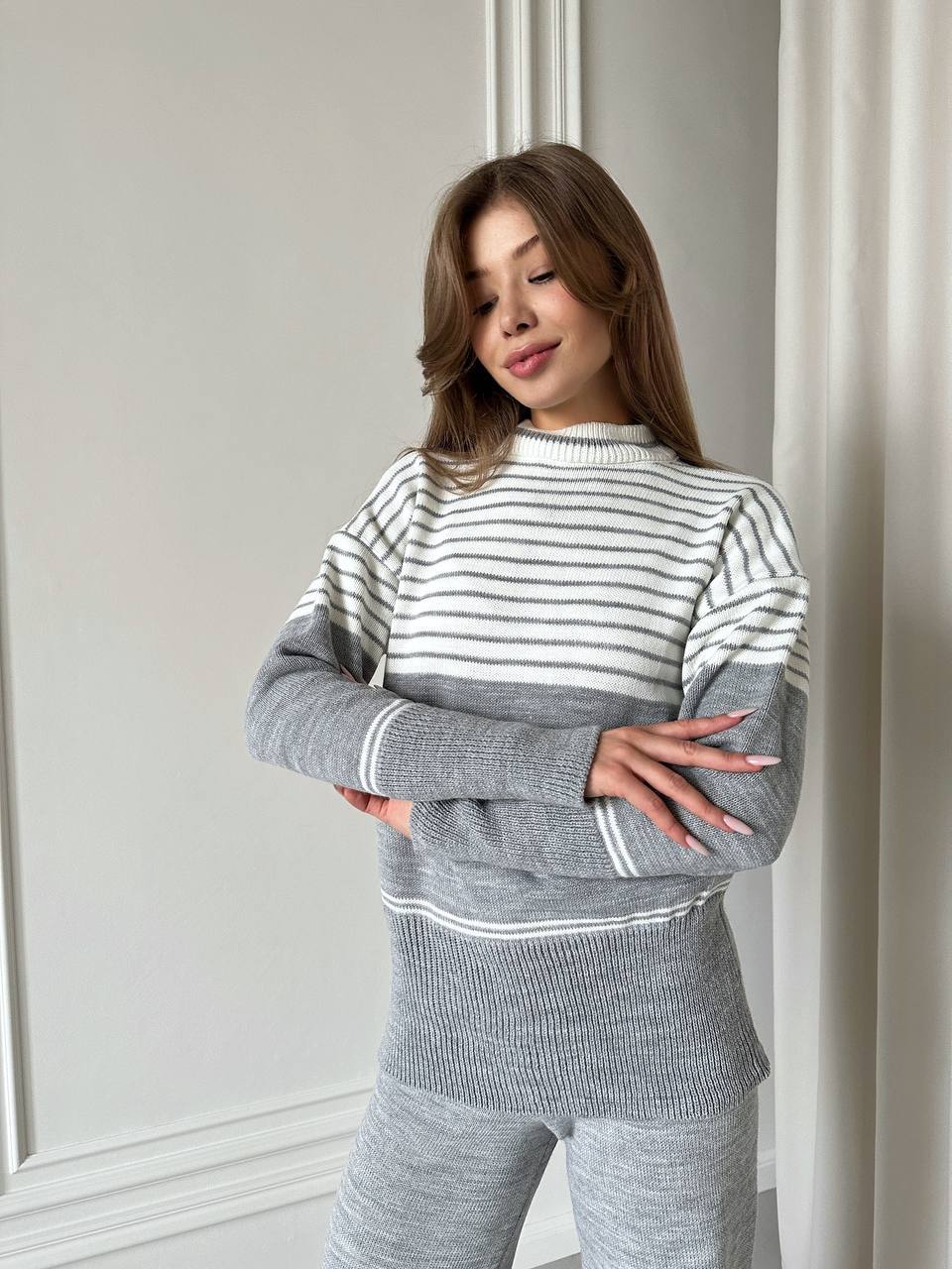 Woman wearing a gray and white striped sweater and pants against a neutral background