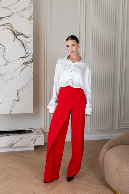 Woman wearing a white blouse and red pants in an indoor setting with marble wall and beige sofa.