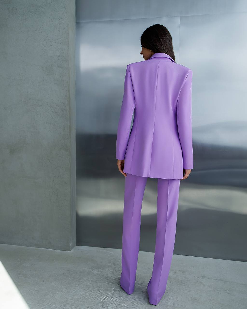 Person wearing a purple suit standing against a gray wall.