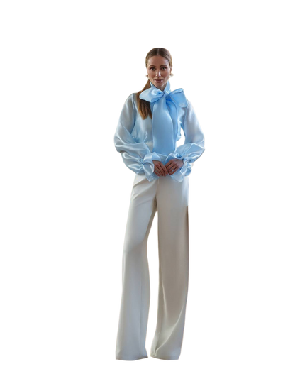 Woman wearing a white blouse with a blue bow and white pants on a white background