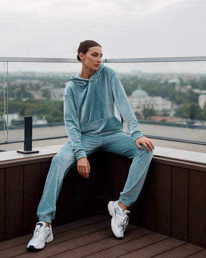 Person wearing a light blue tracksuit sitting on a ledge with a cityscape view.
