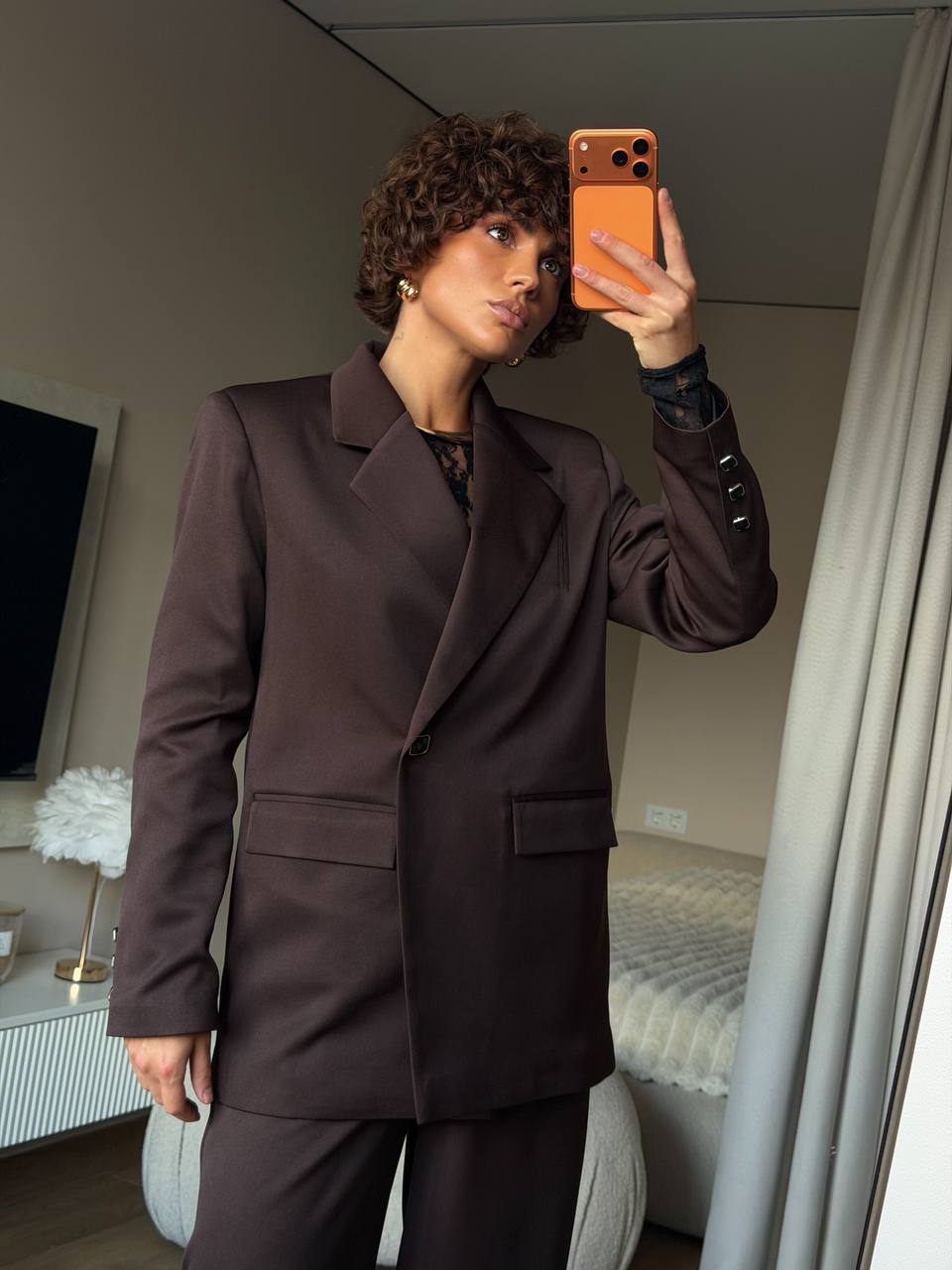 Person taking a mirror selfie wearing a brown coat in a room.