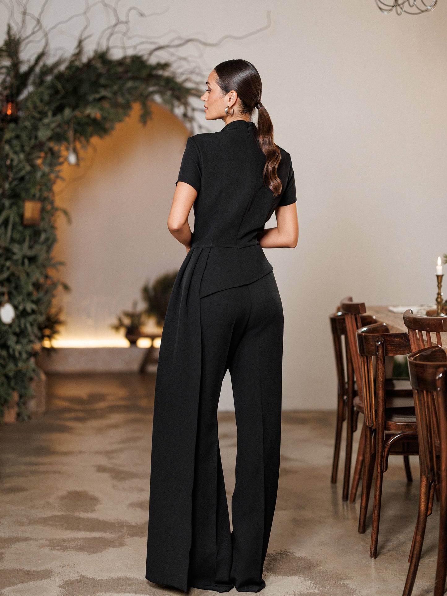 Woman in a black jumpsuit standing in a formal dining room setting.