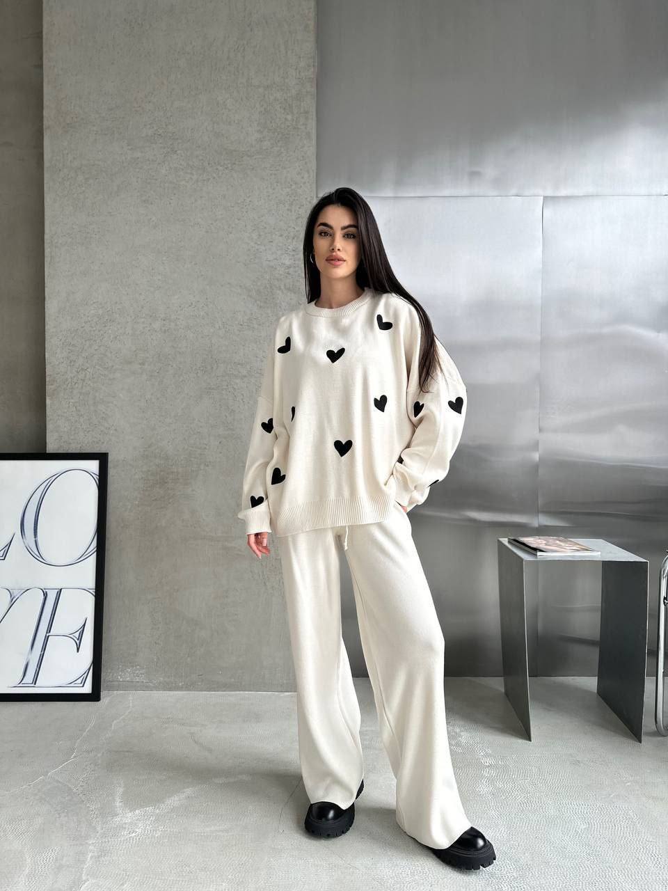 Woman wearing a white outfit with black heart patterns in a minimalistic room.