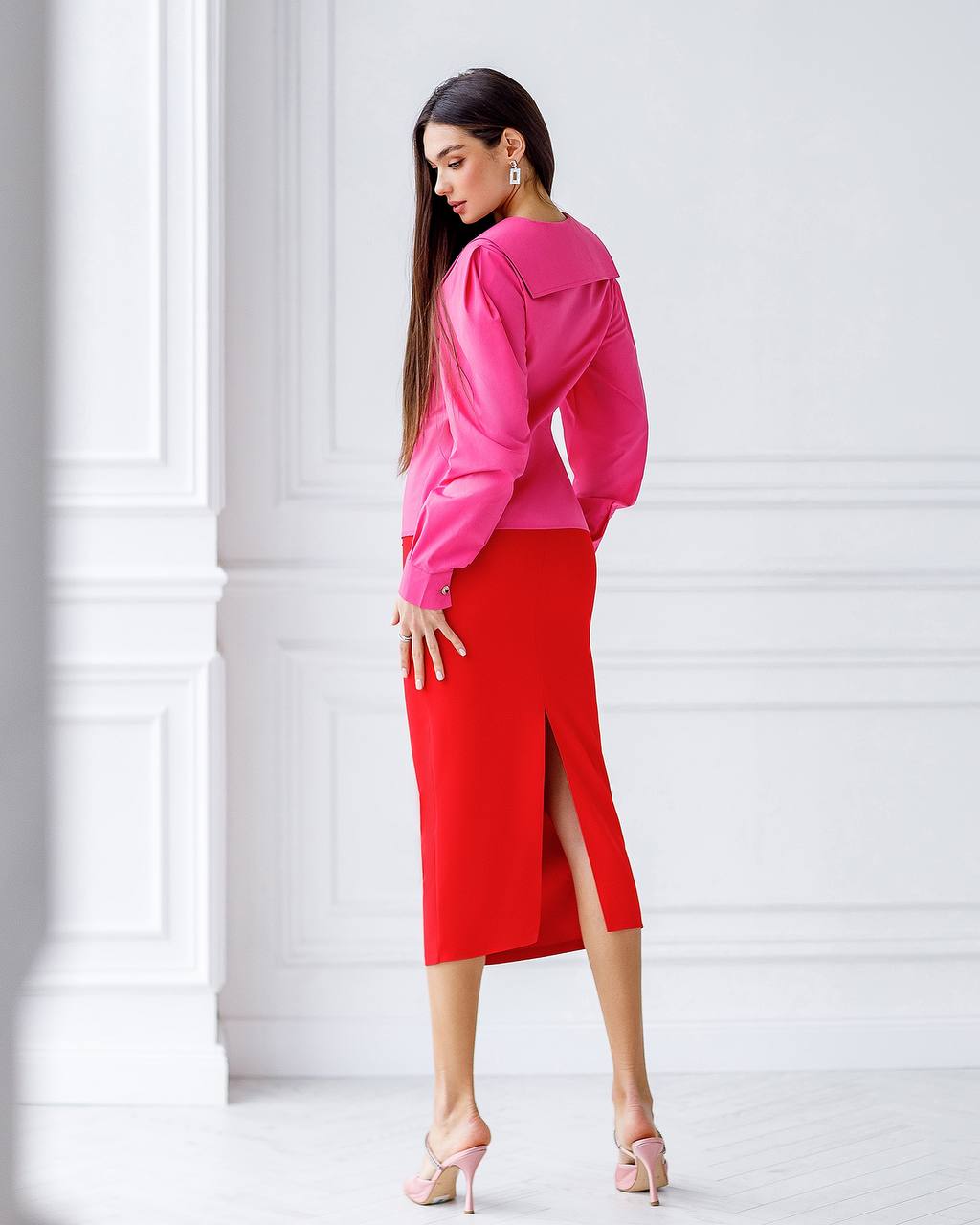 Woman wearing a bright pink blouse and red skirt against a white background