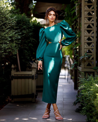 Woman in a teal outfit standing outdoors with greenery around