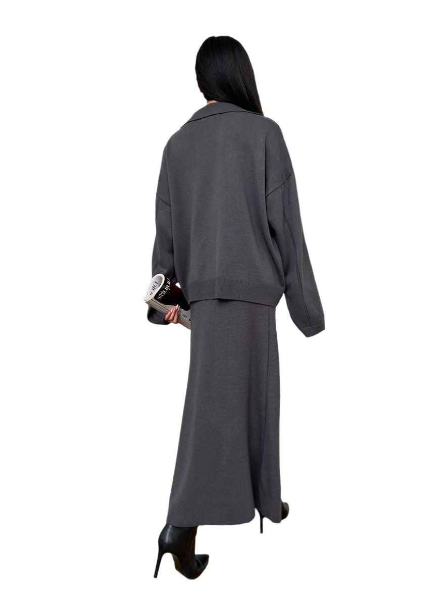 Person wearing a gray outfit with a long skirt and jacket on a white background