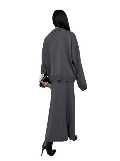 Person wearing a gray outfit with a long skirt and jacket on a white background
