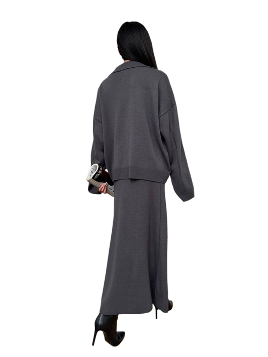 Person wearing a gray outfit with a long skirt and jacket on a white background