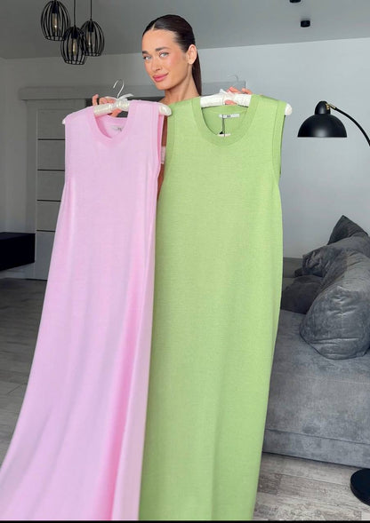 Woman holding two dresses, one pink and one green, in a room with a gray sofa and lamp.
