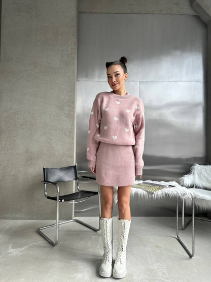 Woman wearing a pink outfit with white hearts in a modern room.