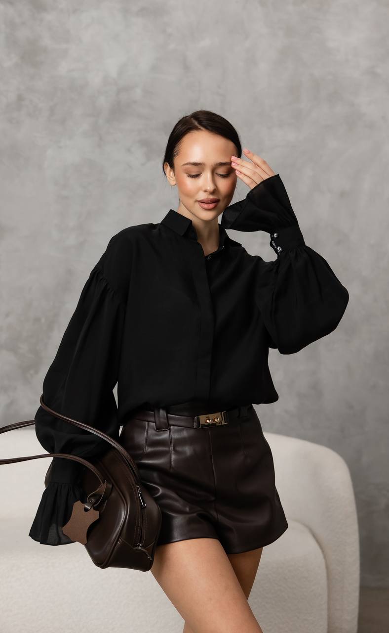 Woman in black outfit with leather skirt holding a brown bag against a gray background