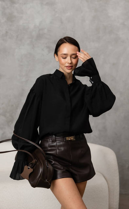 Woman in black outfit with leather skirt holding a brown bag against a gray background