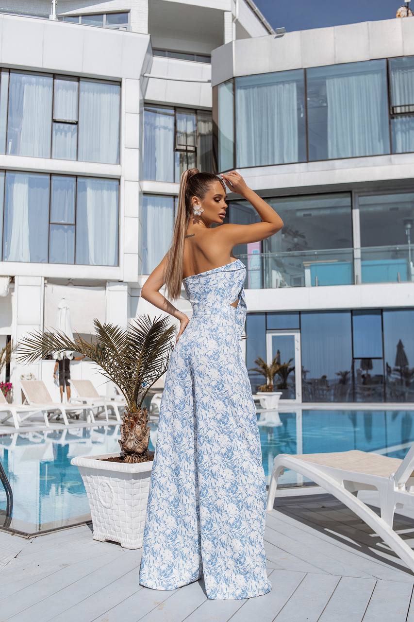Woman in a floral dress standing by a poolside with modern building architecture.