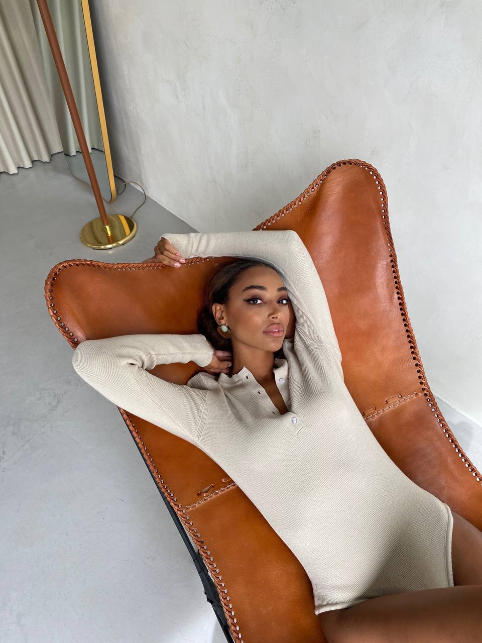 Woman lounging on a brown leather chair in a minimalistic room.